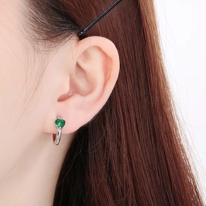 Close-up of heart-shaped green gemstone earring in a polished silver huggie hoop setting