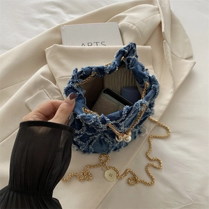 Blue denim bucket bag with gold chain and pearl charm shown in a lifestyle setting