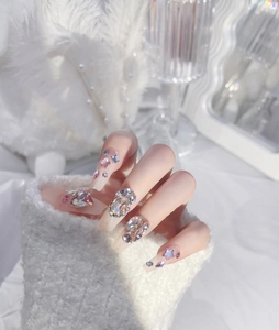 Detail of luxury press-on nails with pink base, star accents, and large heart-shaped diamonds
