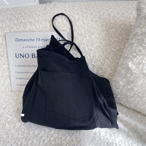 Close-up of black canvas tote bag with large front pocket on white fuzzy background