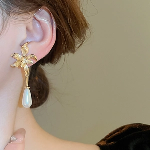Detailed close-up of a model wearing a gold flower earring with a large pearl drop pendant