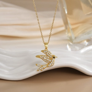 Detailed view of flying bird pendant with zircon pavé setting on a gold cross chain