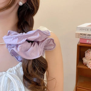 Détail d'un chouchou en tissu violet avec des volants doux sur une coiffure tressée