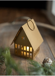 Detail of golden metal house candle holder with hollow stars on dark wood tray with pine
