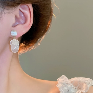 Close-up of elegant gold stud earrings with white circular shell fringe on model