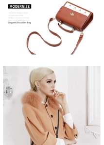 Detail of brown handbag with gold bee ornament and white stitching on synthetic leather