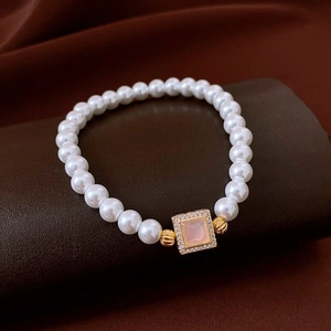 Détail de bracelet en perles blanches avec pendentif doré et pierre rose sur cuir