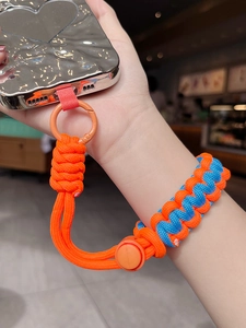 Detail of woven phone wrist strap in orange and blue with silver heart case