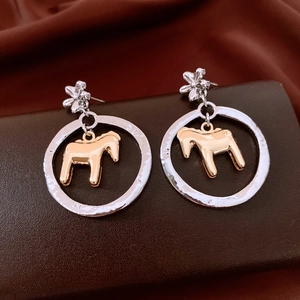 Detailed close-up of silver flower stud earrings with gold horse charm in round circle