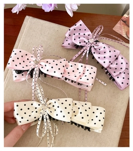 Détail de trois barrettes à nœuds en satin à pois en couleurs rose, violette et crème.