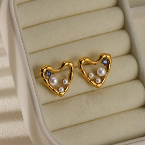 Detail of gold heart earrings with white pearls and a blue gemstone in a jewelry box