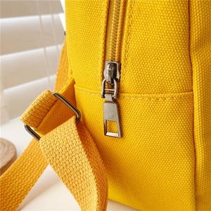 Close-up of yellow canvas backpack showing zipper detail and strap stitching