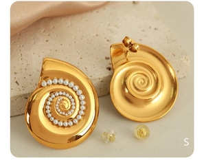 Macro view of gold plated spiral shell earrings with small white pearls on silk background