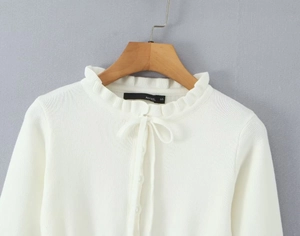 Dettaglio del colletto in maglia bianca con volant e fiocco in nastro coordinato