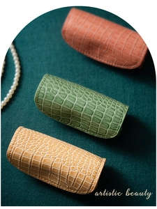 Tre astucci per gioielli in pelle a coccodrillo arancione, verde e beige su velluto verde