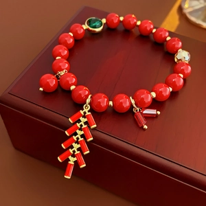 Gros plan d'un bracelet en perles rouges avec des breloques de pétards dorés sur bois