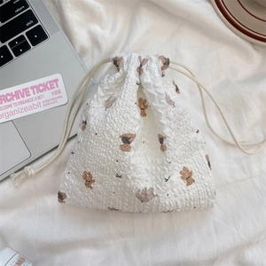 Detail of white drawstring storage bag with brown bear print on textured fabric surface