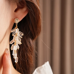 Close-up of golden wheat ear earrings with clear crystals worn by a model in soft lighting