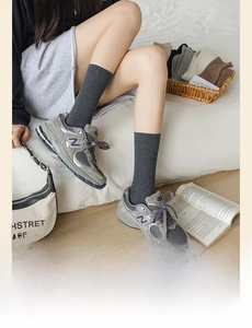 Detail of dark grey ribbed knit crew socks paired with retro sneakers on a soft white bed