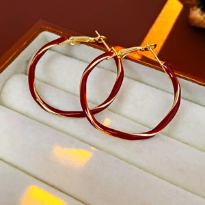 Detail of gold twisted hoop earrings with red enamel finish on a jewelry box