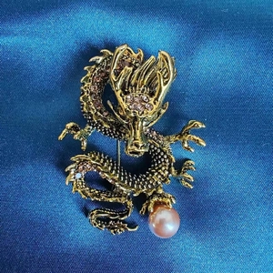 Makroaufnahme der goldenen Drachenbrosche mit rosa Strasssteinen und Perlendetail