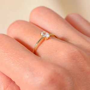 Close-up of minimalist gold ring with oval zircon in a four-prong setting on finger