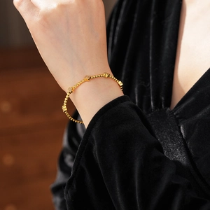 Dettaglio di un bracciale a sfere placcato oro 18k con fiori in zircone sul polso donna