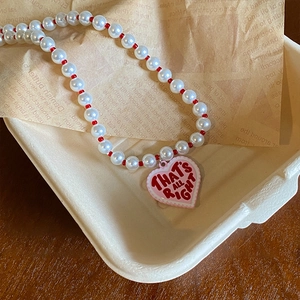 Close-up of pearl necklace with pink heart pendant featuring That's All Right text