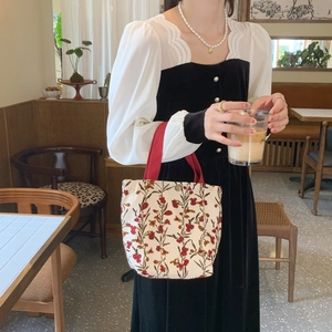 Floral corduroy handbag detail featuring red fabric handles and a secure snap button closure