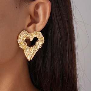 Detailed close-up of chunky gold hollow heart earrings with molten lava texture finish