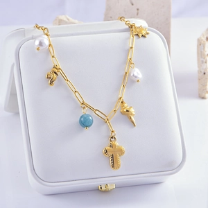 Detail shot of golden necklace featuring cross, seahorse, sun and pearl charms