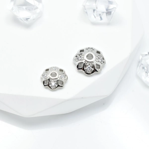 Silver flower-shaped jewelry spacers with zircon stones on white geometric stand