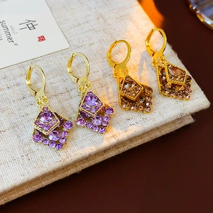 Detail view of gold-plated geometric rhombus earrings with purple and amber crystals