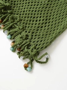 Detailed view of green crochet fabric with colorful bead accents and handmade tassels