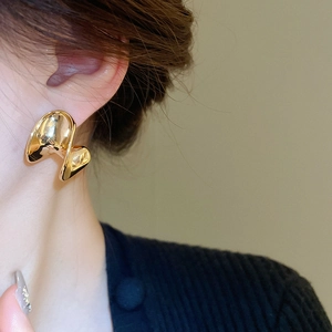 Close-up of a model wearing a twisted gold C-shaped metal stud earring with polished finish
