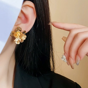 Close-up of golden flower stud earrings with hammered metal texture on a model