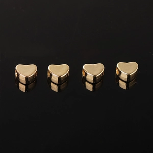 Quattro perline CCB dorate a forma di cuore per gioielli DIY su superficie riflettente
