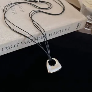 Silver handbag pendant necklace with black cord on velvet background for women