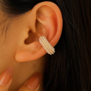 Dettaglio di un ear cuff dorato con file di micro perle bianche indossato sull'orecchio