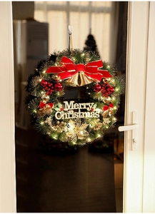 Detail of Christmas wreath with red bow, golden bells, berries and warm LED lights