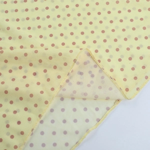 Dettaglio del tessuto in rete giallo chiaro a pois marroni con drappeggio morbido