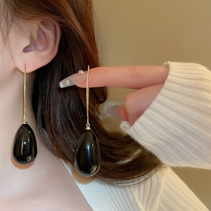 Détail de boucles d'oreilles noires en goutte avec crochets dorés sur un mannequin
