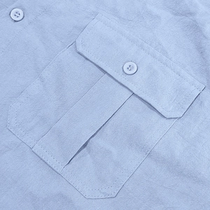 Close-up of light blue linen shirt featuring a buttoned chest pocket and woven texture