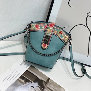 Detail of turquoise bucket bag featuring floral embroidery and metallic turn-lock buckle
