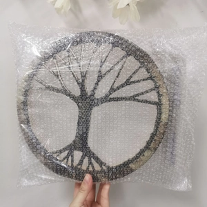 Hand lifting Tree of Life shaman drum wrapped in protective bubble film packaging