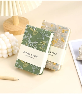 Detailed view of A6 linen notebooks with flower and tree embroidery in green and beige