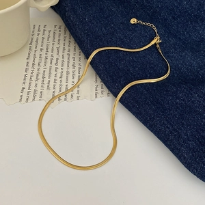 Detailed shot of golden snake bone chain necklace over blue denim with s-curve style
