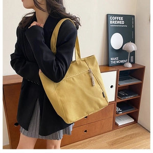 Detail of yellow canvas tote bag with side charm accessory and secure zipper closure