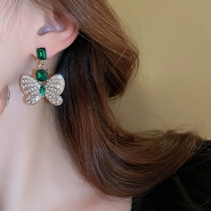 Gros plan de boucles d'oreilles papillon en émeraude et diamants portées par un mannequin