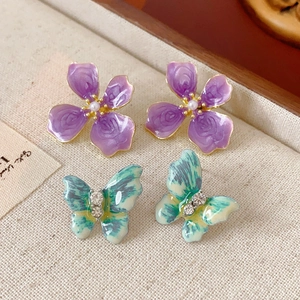 Détail de boucles d'oreilles fleur émaillée violette et papillon avec strass